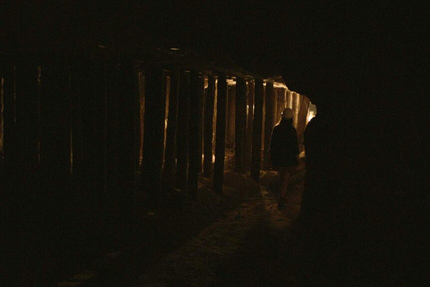 The protganist of the film, wearing a hard hat, walks through a shadowy mineshaft.