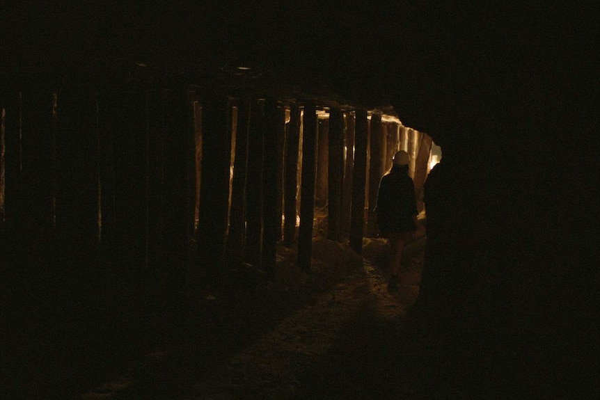 The protganist of the film, wearing a hard hat, walks through a shadowy mineshaft.