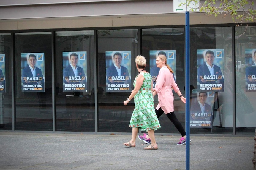 Two women walk past a shop window covered with Basil Zempilas campaign posters