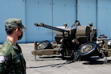 A man in a Taiwanese military uniform watches as soldiers operate a large, double-barrelled cannon on an open concrete space.