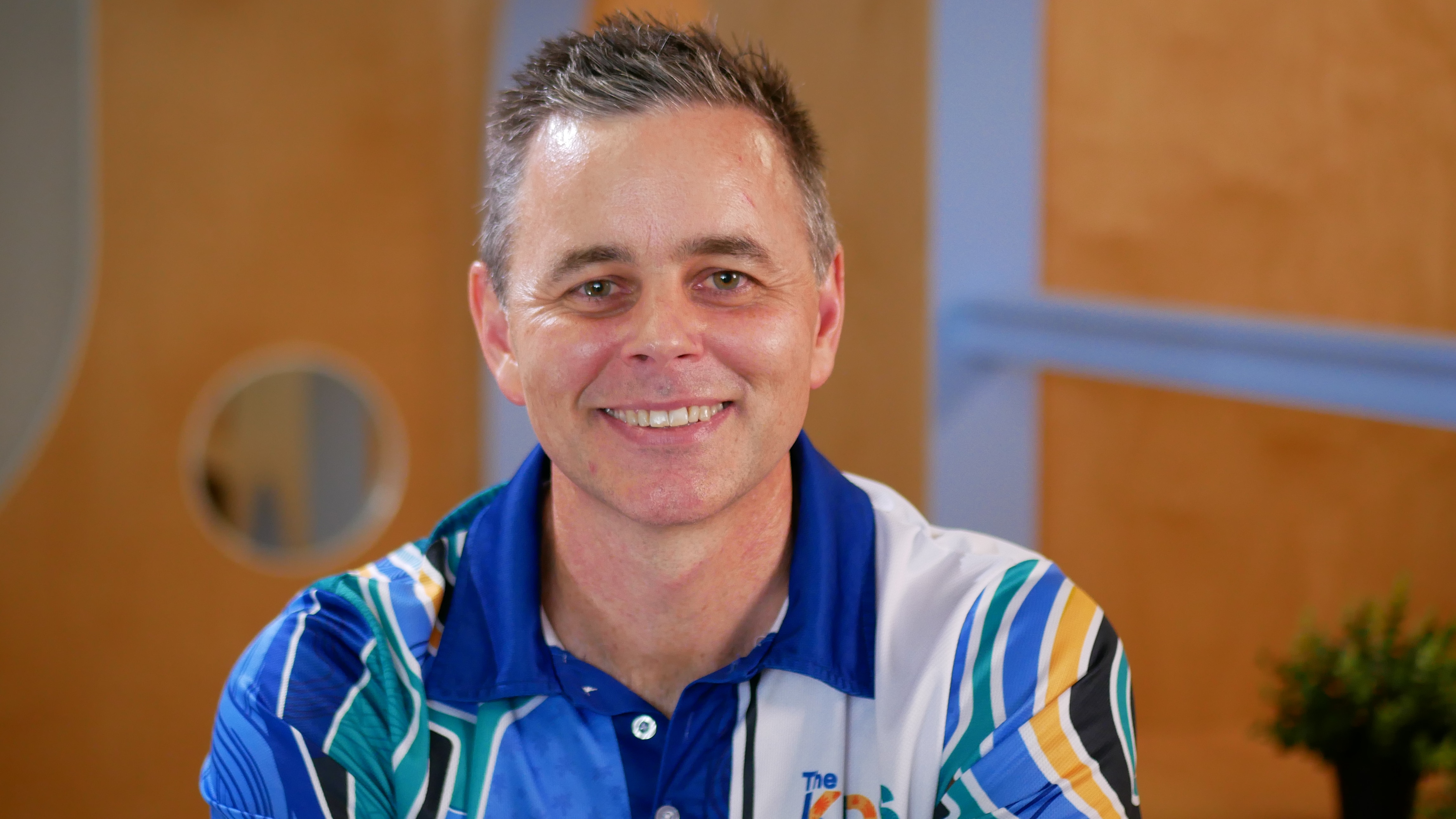 Un hombre blanco con pelo corto se sienta en una oficina y sonríe