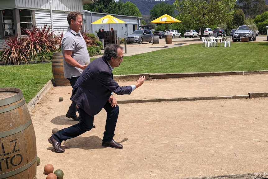 Two men play bowls on a sand strip of ground at the winery
