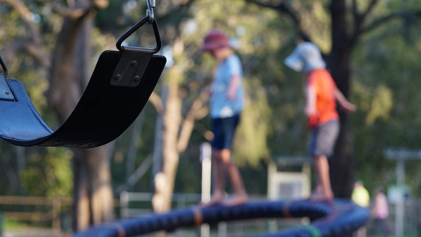 Two anonymous primary school-aged boys walk and balance on playground equipment in a park.