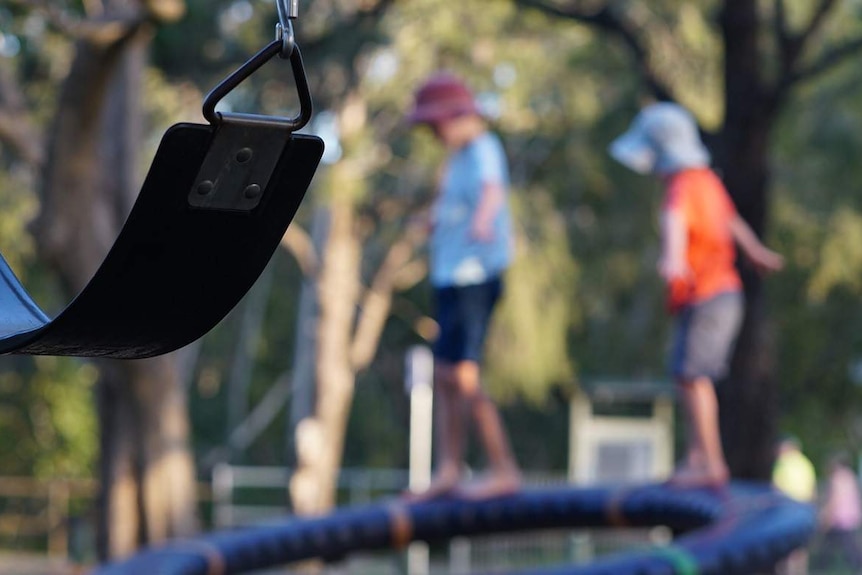 Two anonymous primary school-aged boys walk and balance on playground equipment in a park.