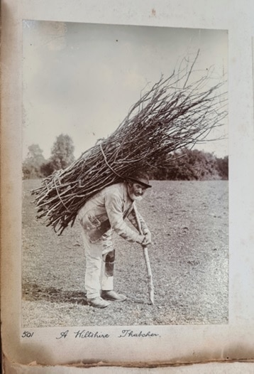 An old photograph showing a man carrying a large bundle of sticks on his back 