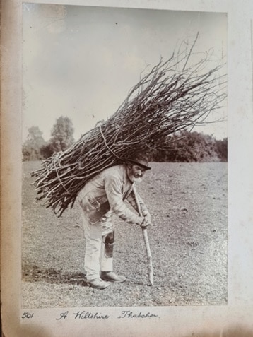 An old photograph showing a man carrying a large bundle of sticks on his back 