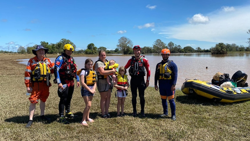 people standing together earing life jackets with an inflatable rescue boat with floodwater in the background