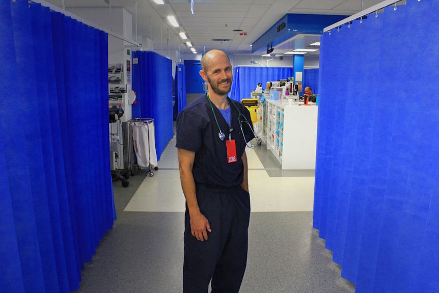 Jason Quinn dressed in blue scrubs inside a hospital hallway
