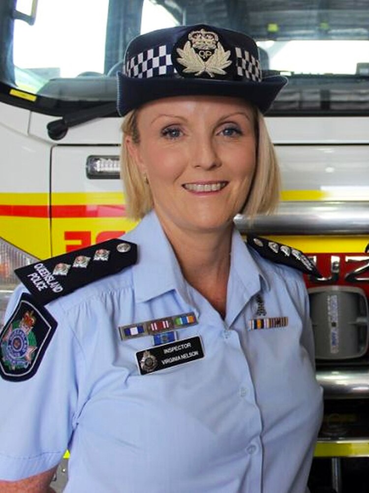 A female police officer with short blonde hair poses for a photo in her blue uniform, in front of a fire truck