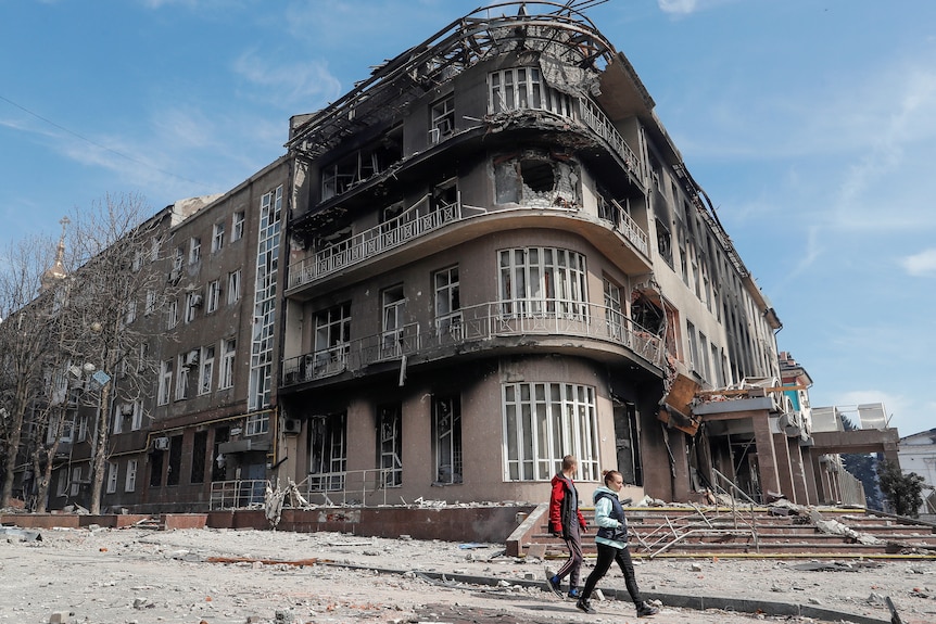 Residents walk near a bombed out building in Mariupol