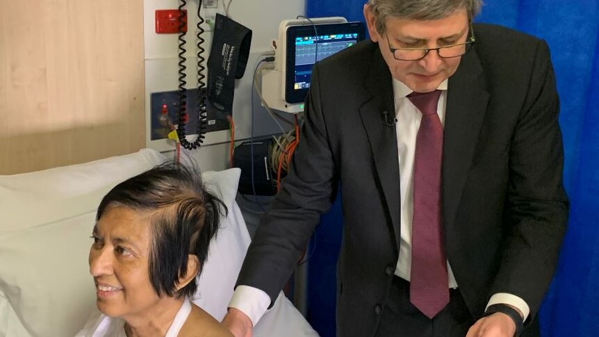 A man looking at a mobile phone screen as he holds a small monitor against a female patient's back.