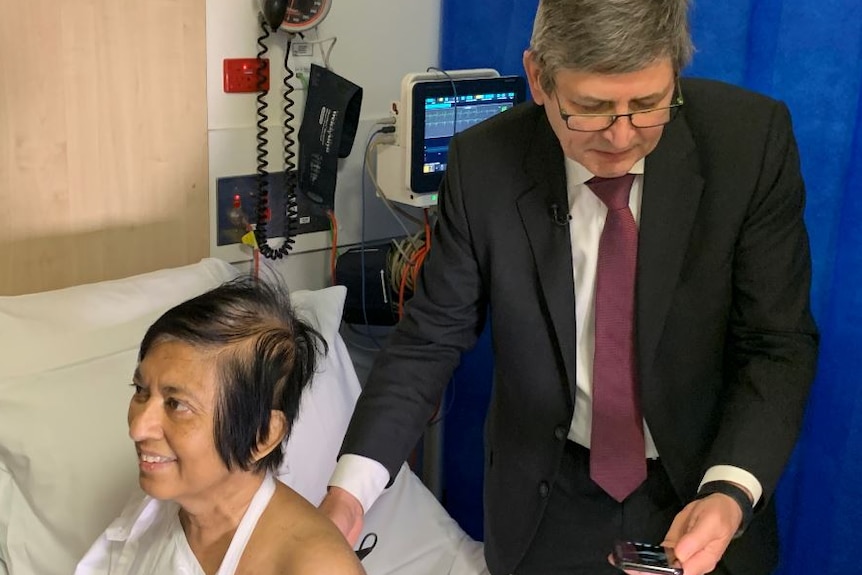 A man looking at a mobile phone screen as he holds a small monitor against a female patient's back.