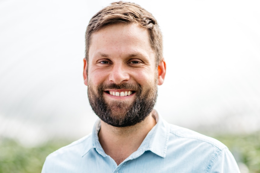 A man with a beard is smiling at the camera with a blue shirt on