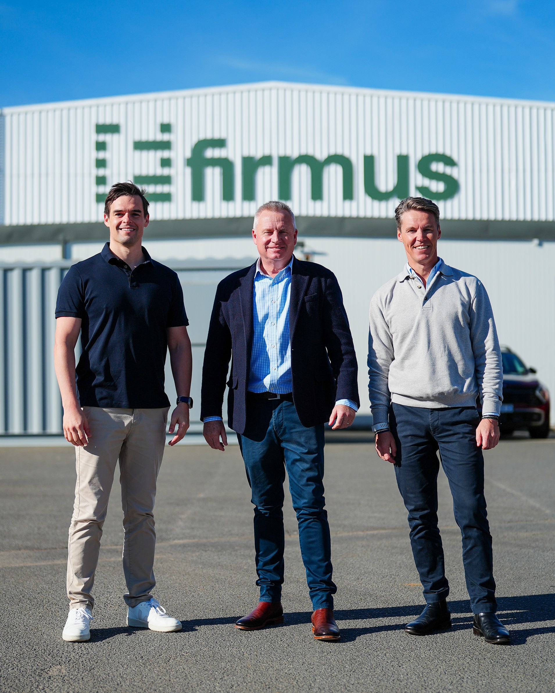Three men standing outside a building that says 'Firmus'.