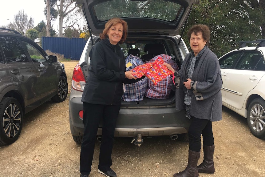 Two women stand in front of a car filled with bags containing period kits.