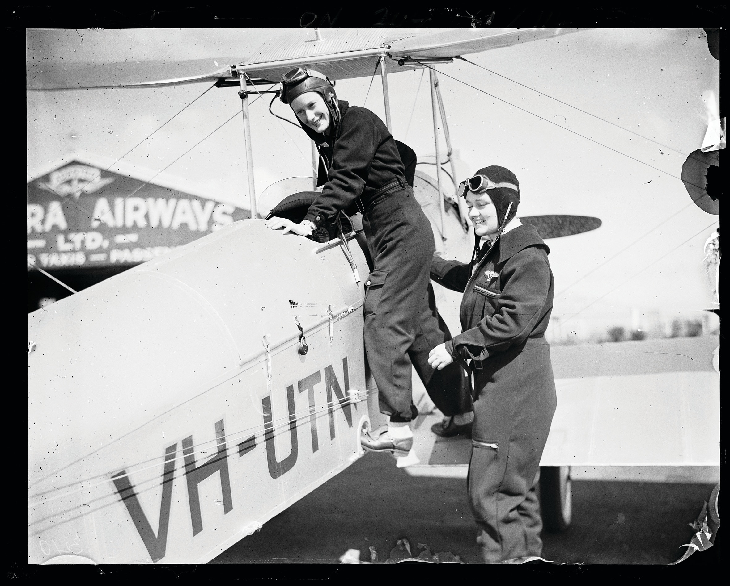 Black and white image of two women at the cockpit of a biplane.