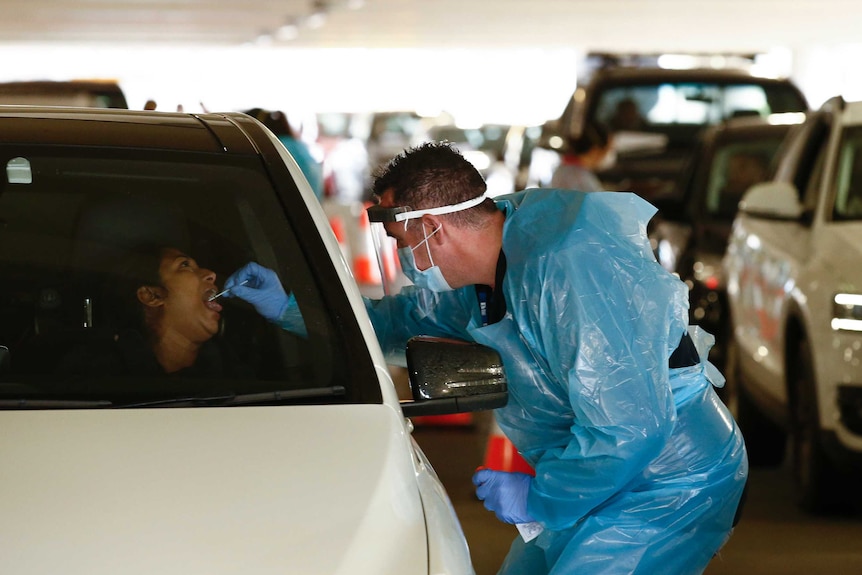 A medical worker swabs the mouth of a car driver through the car window.