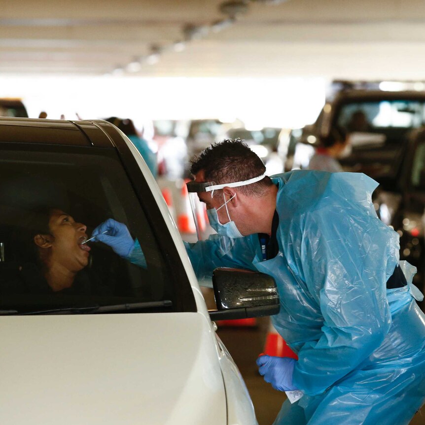 A medical worker swabs the mouth of a car driver through the car window.