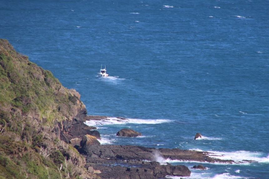 A boat travels past a steep cliff.