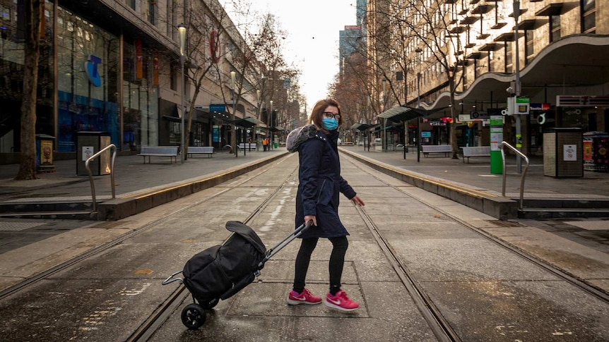 A woman with a bag crosses an empty Melbourne CBD street.