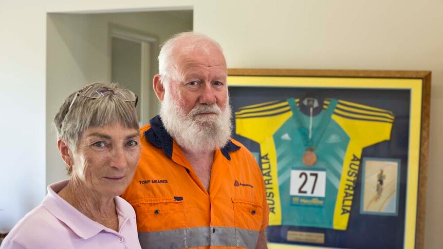 Marilyn and Tony Meares stand next to each other with Anna Meares' medal framed in the background