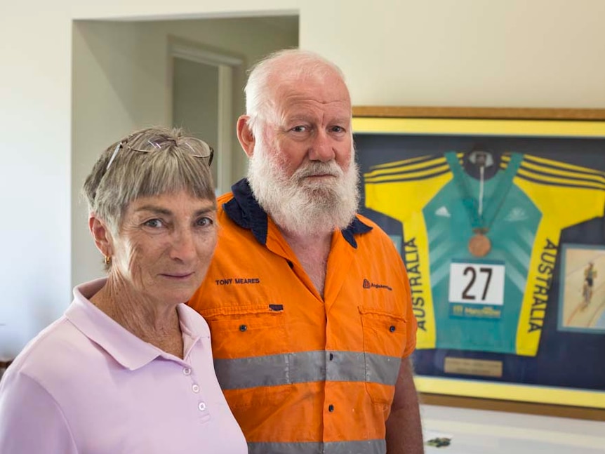 Marilyn and Tony Meares stand next to each other with Anna Meares' medal framed in the background