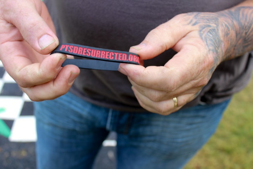 A man holds a PTSD Resurrected wristband.  