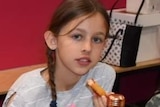 A young girl in a grey and white striped shirt with a side braid.