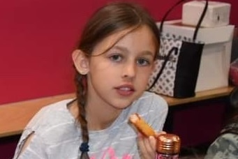 A young girl in a grey and white striped shirt with a side braid.