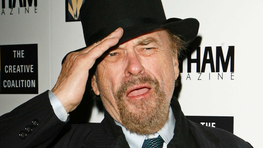 Rip Torn salutes at a red carpet event in front of a sponsor's backdrop