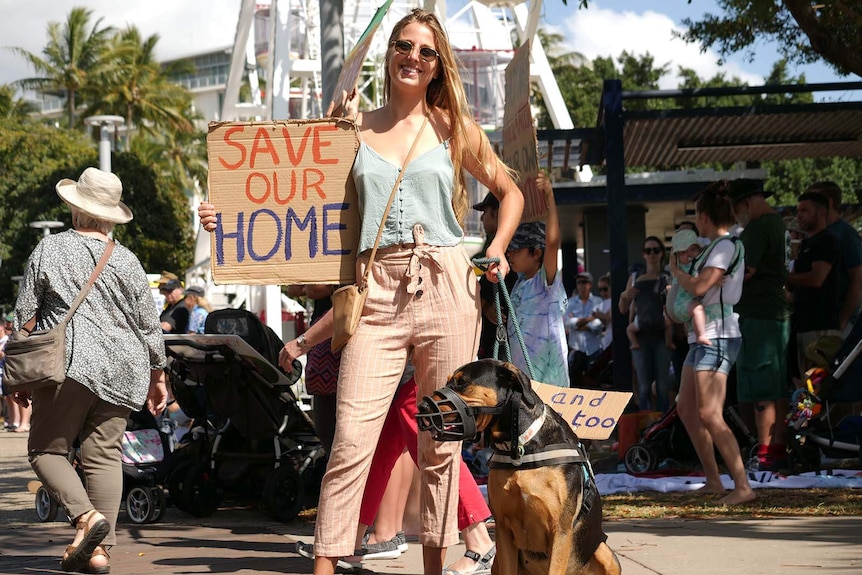 A young woman marching with her muzzled dog, and holding a placard