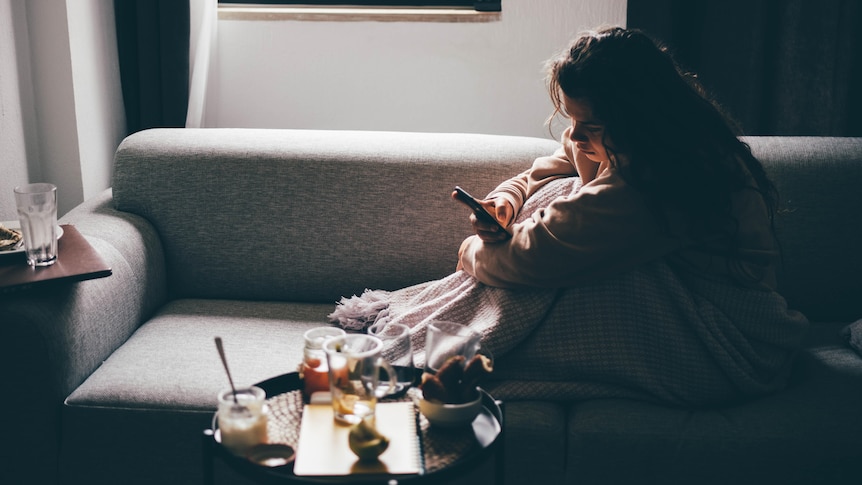 Woman looking at her phone on the couch surrounded by dirty dishes