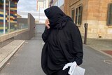 A woman wearing a black hijab holding a plastic bag