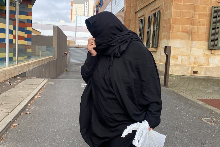A woman wearing a black hijab holding a plastic bag