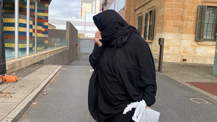 A woman wearing a black hijab holding a plastic bag