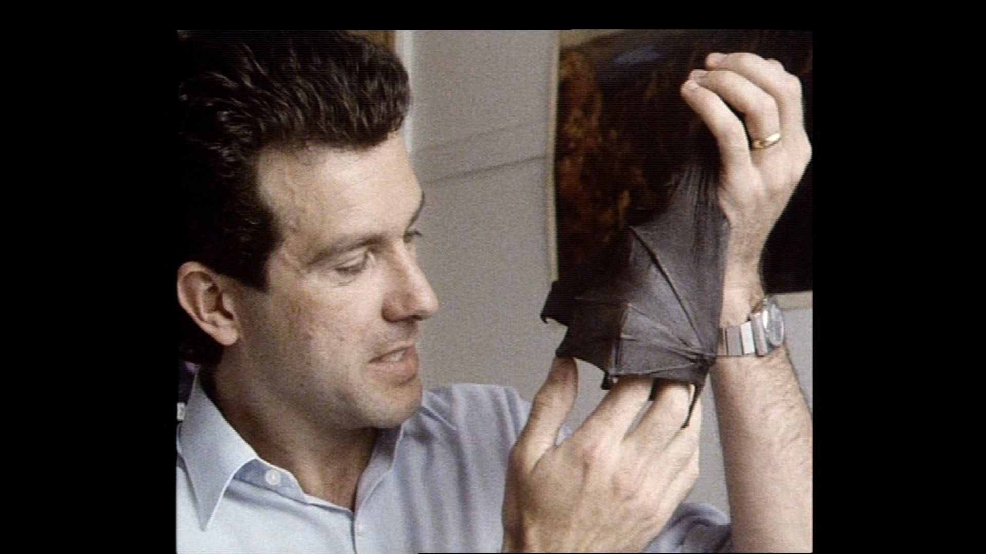 Morecroft in a work shirt with a small bat hanging from his finger inside a room.