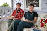 Daniel and Linda, who both wear glasses and tattoos, sitting on their porch with a cup of tea.