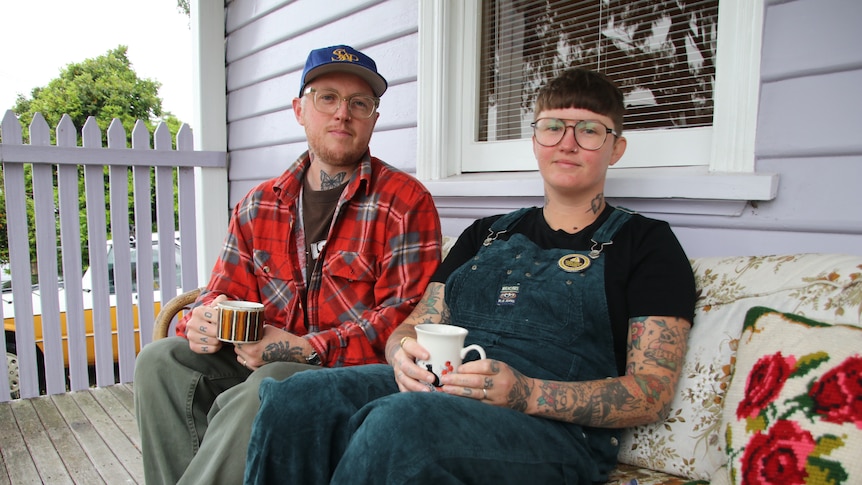 Daniel and Linda, who both wear glasses and tattoos, sitting on their porch with a cup of tea.