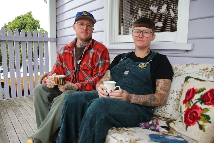 Daniel and Linda, who both wear glasses and tattoos, sitting on their porch with a cup of tea.