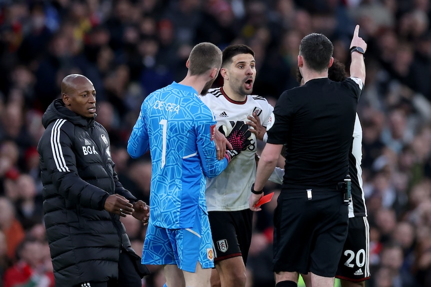 A goalkeeper tries to calm a forward down as he shouts at the referee who is pointing to send him off in the FA Cup.