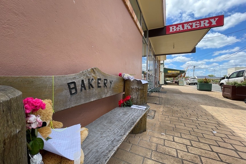 A teddy bear and other tributes sit on a chair in front of the Biggenden bakery. 
