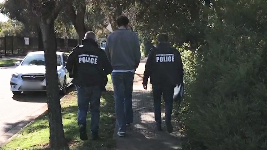 Two AFP officers escort a tall man wearing jeans and a jumper 