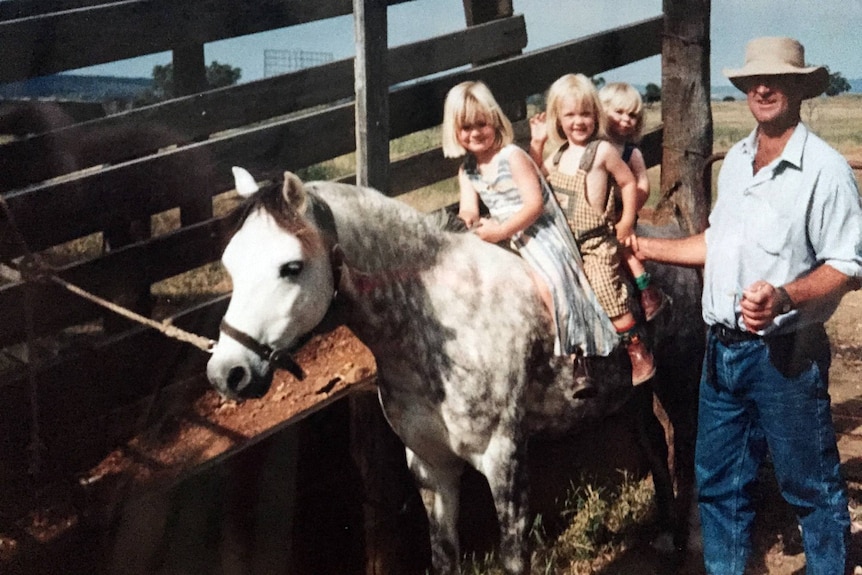 A photo of three little girls sitting on a dapple grey horse.