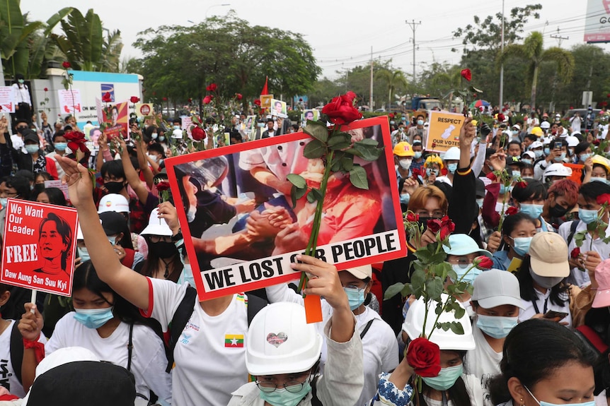 A protester holds an image of a woman and a rose with a sign that reads "We Lost Our People" during a large protest.