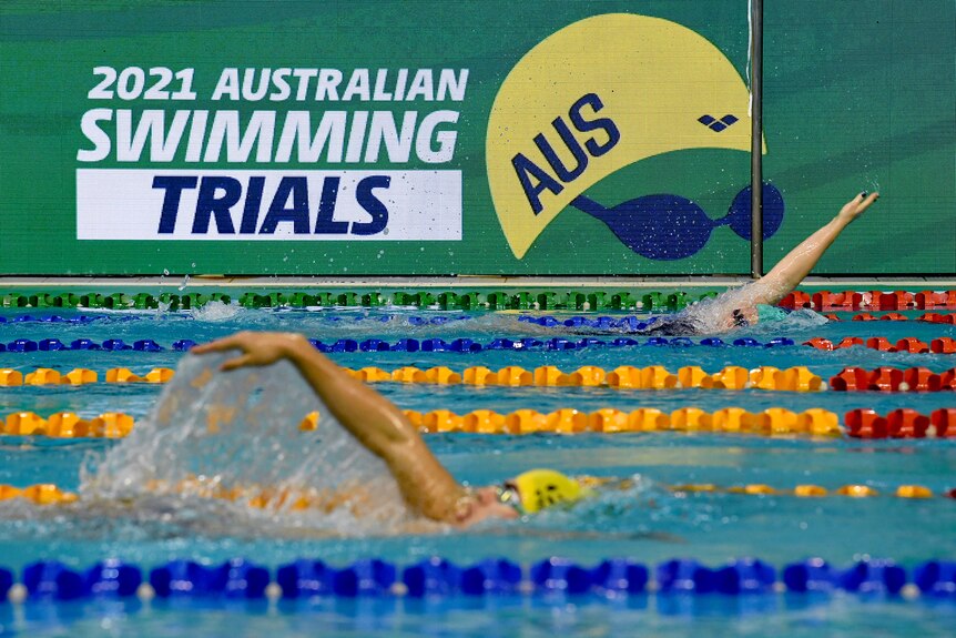 Les nageurs font leurs pas dans la piscine tandis qu'à l'arrière-plan se trouve un grand panneau "Essais de natation australiens 2021".