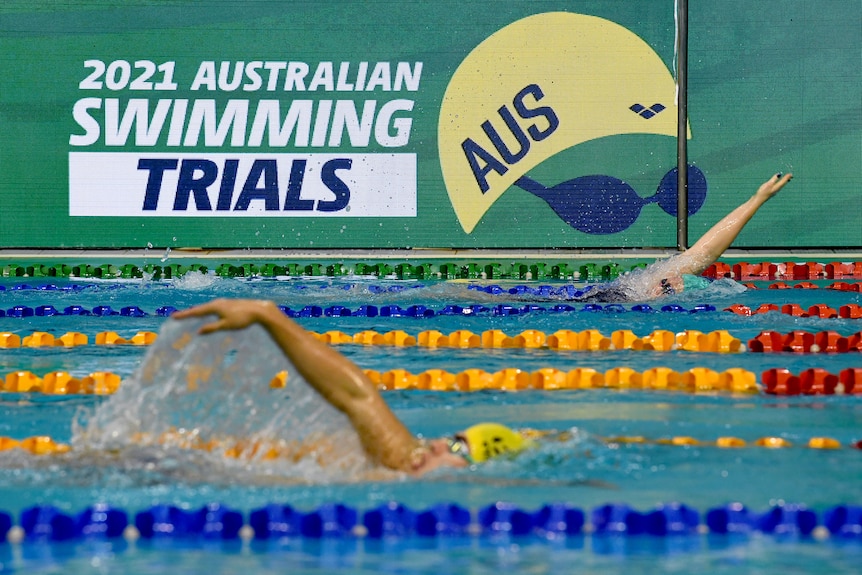 Swimmers go through their paces in the pool while in the background lies a big sign "2021 Australian Swimming Trials".