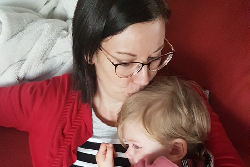 A woman kisses her young son on the sofa while she cradles him.