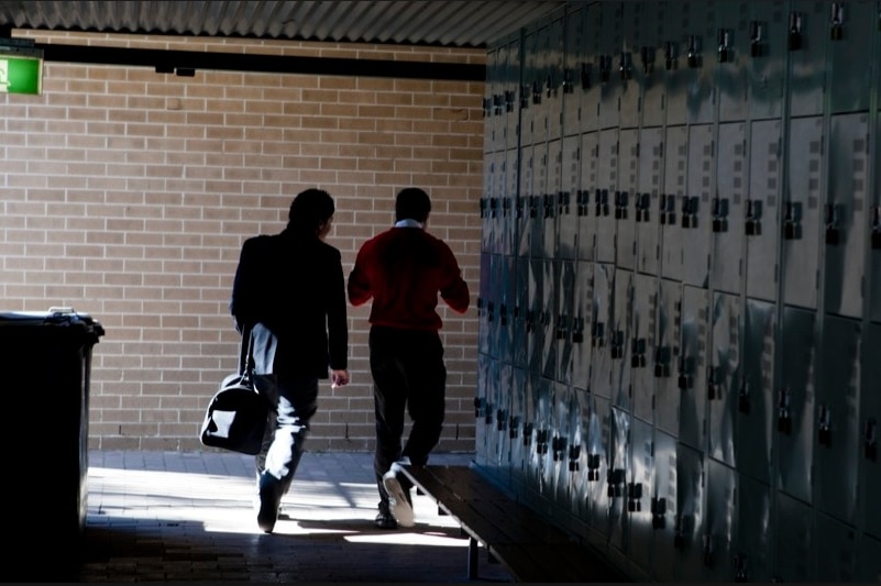 Two children walk past some lockers at a school.