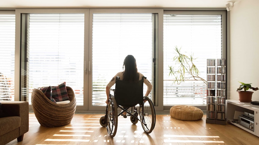 An unidentifiable woman in a wheelchair at home on her own.