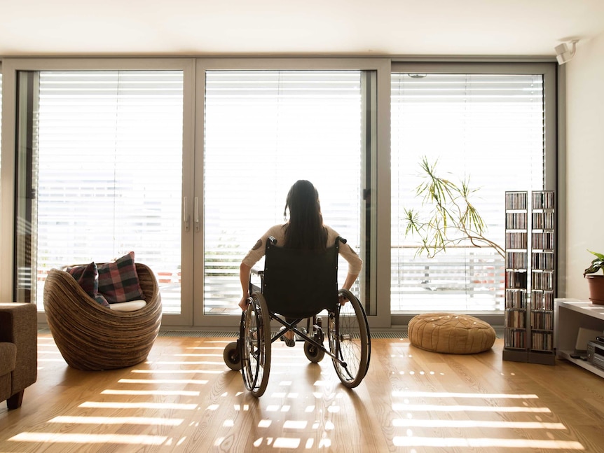 An unidentifiable woman in a wheelchair at home on her own.